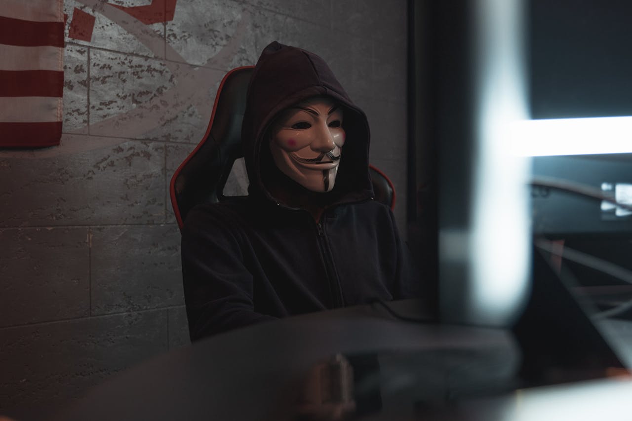 A mysterious person in a Guy Fawkes mask working at a computer, symbolizing cyber security themes.